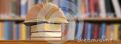 open book that lies on a stack of books against the background of bookshelves Stock Photo