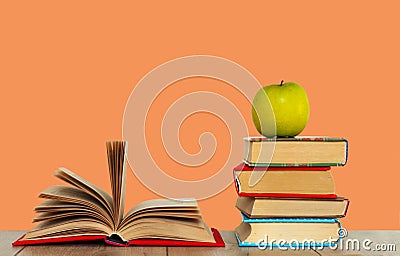 Open book textbook, pile of books and green apple on a wooden desk on the pink orange background. Back to school distance home Stock Photo