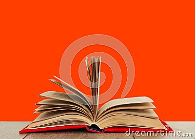 Open book textbook in a red cover on a wooden desk with orange background. Back to school distance home education.Quarantine Stock Photo