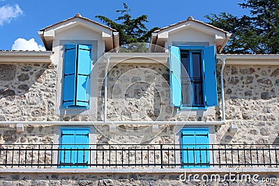 Open and closed light blue wooden window blinds on windows of newly built Mediterranean villa in traditional stone style with Stock Photo