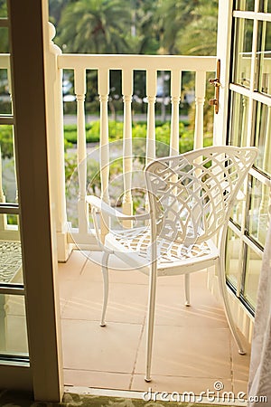 Open door to the balcony, where there is a white forged chair Stock Photo
