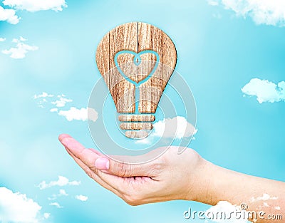 Open female hand with Heart in lightbulb wood icon with blue sky Stock Photo