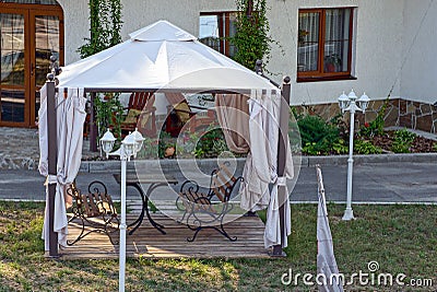 Open gazebo with benches on the lawn with lanterns near the road Stock Photo