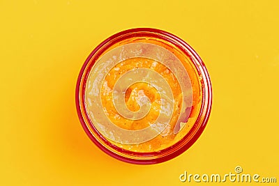 An open glass jar with an orange facial scrub is on a yellow background. Stock Photo