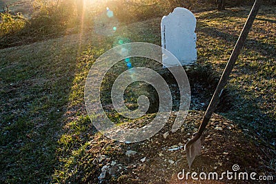 Open grave with shovel at sunset Stock Photo