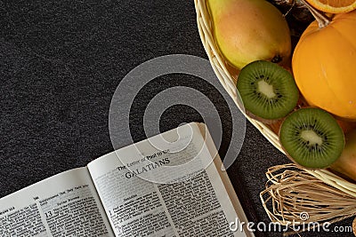 An open Holy Bible book of Galatians with a wicker basket full of various fresh fruits with copy space Stock Photo