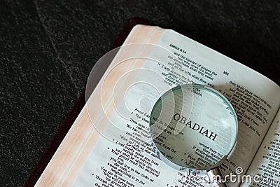 Open Holy Bible Book Old Testament Obadiah prophet with a magnifying glass on dark granite background Stock Photo