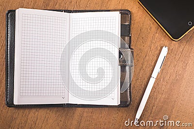 An open leather notebook with a white pen and a telephone lie on a wooden table Stock Photo