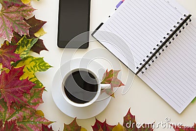 Open notebook, mobile phone and cup of coffee, framed with autumn leaves on white background. Flat lay. Top view. Empty Stock Photo