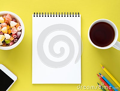 Open notepad on spiral with clean white page, cup with tea, caramels in a bowl, smartphone and color pencil Stock Photo