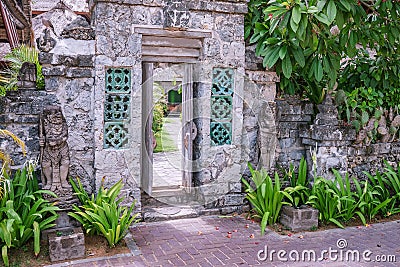 Open old wooden entry doors in stone wall with two traditional Balinese guard statues, street photo Stock Photo