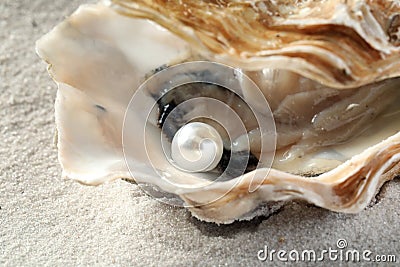 Open oyster with white pearl on sand, closeup Stock Photo