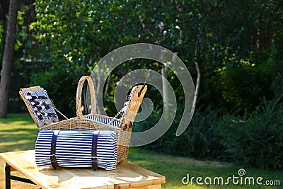 Open picnic basket with blanket on wooden table in green park Stock Photo