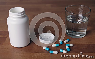 Open pill bottle with blue capsules beside a glas water. Stock Photo