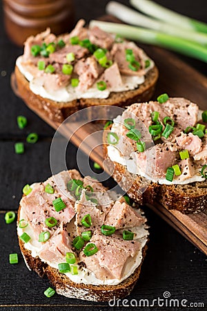 Open sandwiches with cottage cheese, canned tuna and green onions on black wooden background. Stock Photo