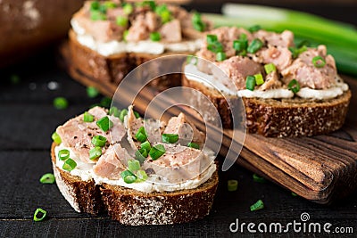 Open sandwiches with cottage cheese, canned tuna and green onions on black wooden background. Stock Photo