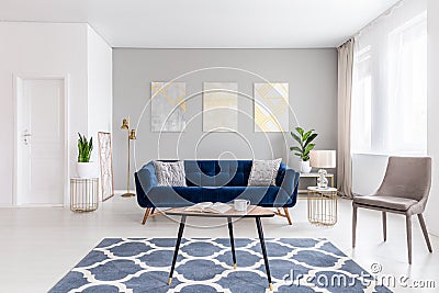 Open space living room interior with modern furniture of a navy blue settee, a beige armchair, a coffee table and other objects in Stock Photo