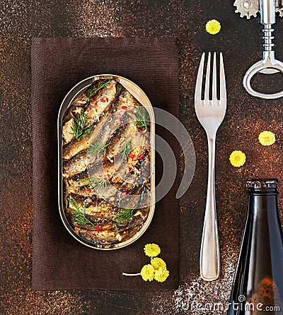 Open tin of Baltic sprats in oil with spices with a fork and a bottle of dark beer on an old brown background Stock Photo