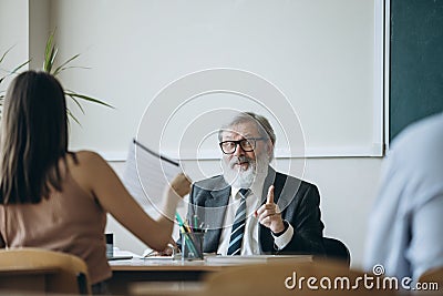 Elderly gray-headed man, professor, teacher and students at lecture, lesson at classroom, indoors. Concept of Stock Photo