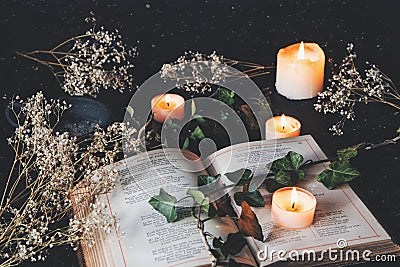 Open vintage poetry book on a black table surface with white lit burning candles and dried flowers Stock Photo