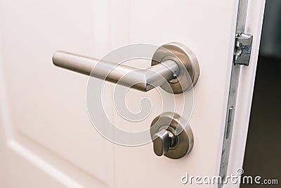 Open the white door. Modern chrome handle in your hotel room or home. Entrance to an apartment, office, or bedroom. Door detail. Stock Photo