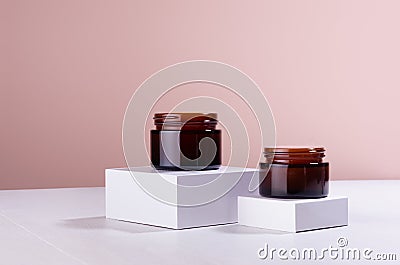 Opened brown cosmetics containers for moisturizer cream on white podium with beige wall, mockup. Template for branding identity. Stock Photo