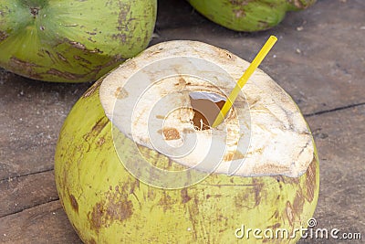 Opened coconut with straw ready for drinking. Fresh coco water photo. Coconut fruit on wooden table. Stock Photo