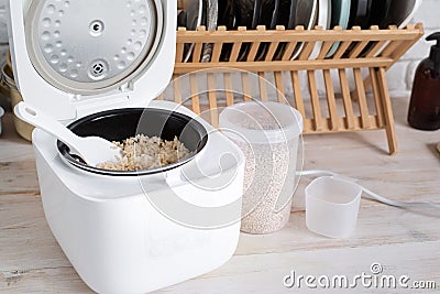 Opened electric rice cooker with cooked steaming brown rice on wooden counter-top in the kitchen Stock Photo