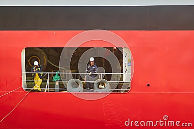 Opened flap in the hull of a huge freighter, from which Asian ship workers look out over the land as they pass through the lock Editorial Stock Photo