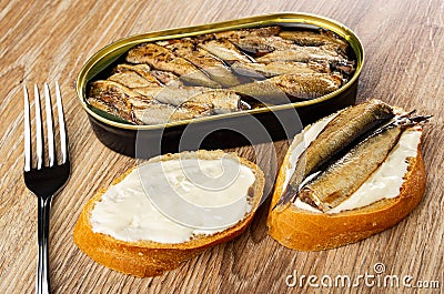 Opened jar with sprats, fork, slice of bread with mayonnaise, sandwich with sprats on wooden table Stock Photo