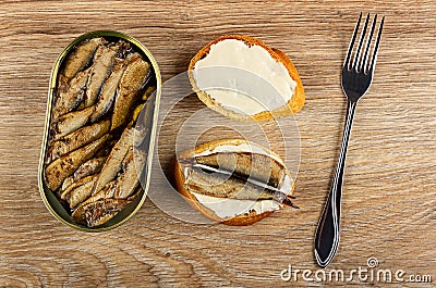 Opened jar with sprats, slice of bread with mayonnaise, sandwich with sprats, fork on wooden table. Top view Stock Photo