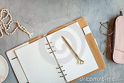 Opened notebook with clean sheets, gold pen, rosary, pink colored case and cup of tea near vase Stock Photo