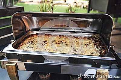 Opened stainless hotel pans on food warmer with baked meal. Self-service buffet table. Celebration, party, birthday or Stock Photo
