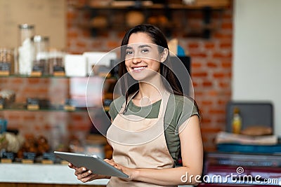 Opening small business. Happy arab woman in apron near bar counter holding digital tablet and looking at camera Stock Photo