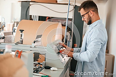 Operating printing cutting machine. Print house worker in white clothes is indoors Stock Photo