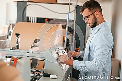 Operating printing cutting machine. Print house worker in white clothes is indoors Stock Photo