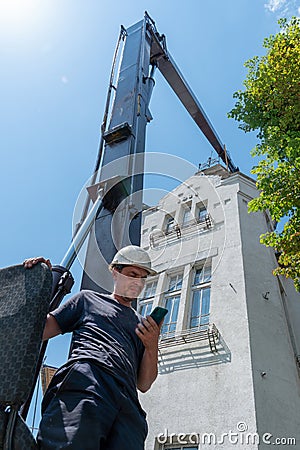 The operator of the tower crane in a helmet and overalls stands next to the controls and instruments. The builder poses Stock Photo