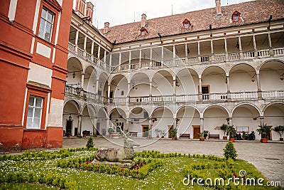 Opocno castle, renaissance chateau, courtyard with arcades and red facade, green lawn with statue and flowers in foreground, sunny Editorial Stock Photo