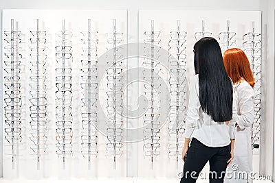 Optician and a brunette client standing in fron of the windoe with many glasses Stock Photo