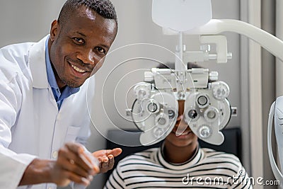 Optician Doing Optometry Eye Exam For Black African teen girl Patient. Male optometrist with phoropter while examining patient Stock Photo