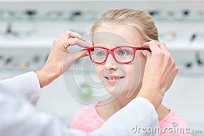 Optician putting glasses to girl at optics store Stock Photo