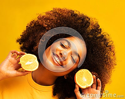 Optimist Young female model of afro appearance. Clean, even skin of the face. In the hands of citrus, orange. Stock Photo