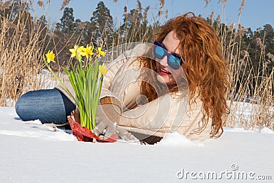 Optimistic curly haired woman admiring bouquet of yellow narcissus while lying in snow Stock Photo