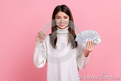 Optimistic dark haired woman holding bitcoin and big fan of dollar bills, exchange crypto currency. Stock Photo