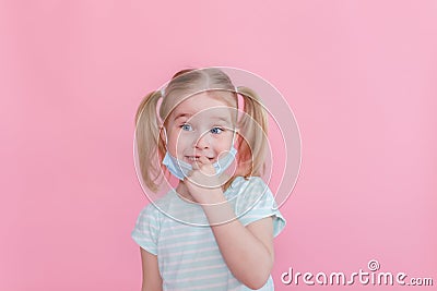 Optimistic, smiling happy little girl taking off the medical mask from face on a pink background showing end of the pandemia. Stock Photo