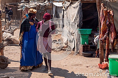 Old Woman in Traditional Herero Clothing and Young Schoolgirl in School Uniform on the local Market in Opuwo Editorial Stock Photo