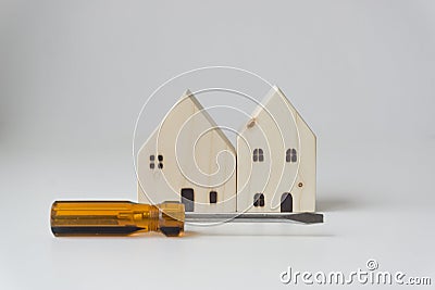 Orange-black screwdriver placed in front of 2 small white wooden houses.White background. Home improvement ideas Stock Photo