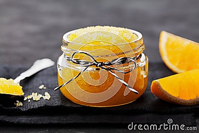 Orange body scrub with sugar and coconut oil in glass jar on black table. Homemade cosmetic for peeling and spa care Stock Photo