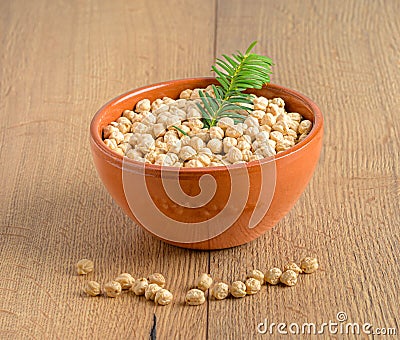 Orange bowl full of chickpeas Legume with plant on wooden background Stock Photo