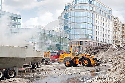 Orange bulldozer loads wet snow to trucks for snow melting Stock Photo